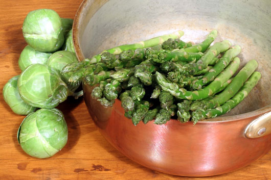 copper pot and green vegetables on a wood counter