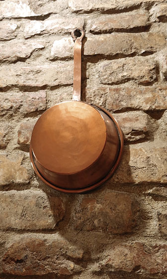 antique copper pot hanging on a brick wall